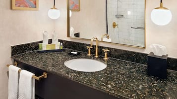 A bathroom with a marble countertop, gold fixtures, a large mirror, and a towel rack.