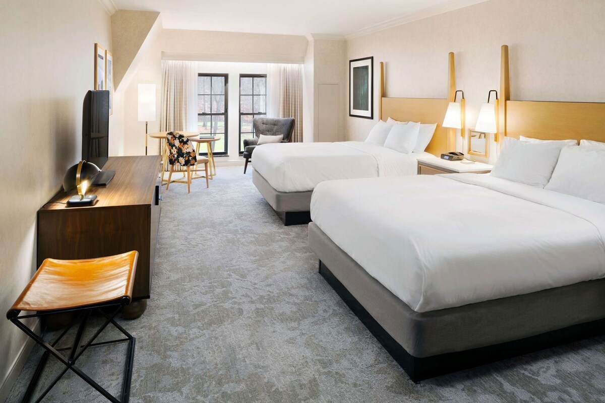 Une chambre d’hôtel avec deux lits, un bureau, une chaise, une télévision et une fenêtre avec des rideaux.