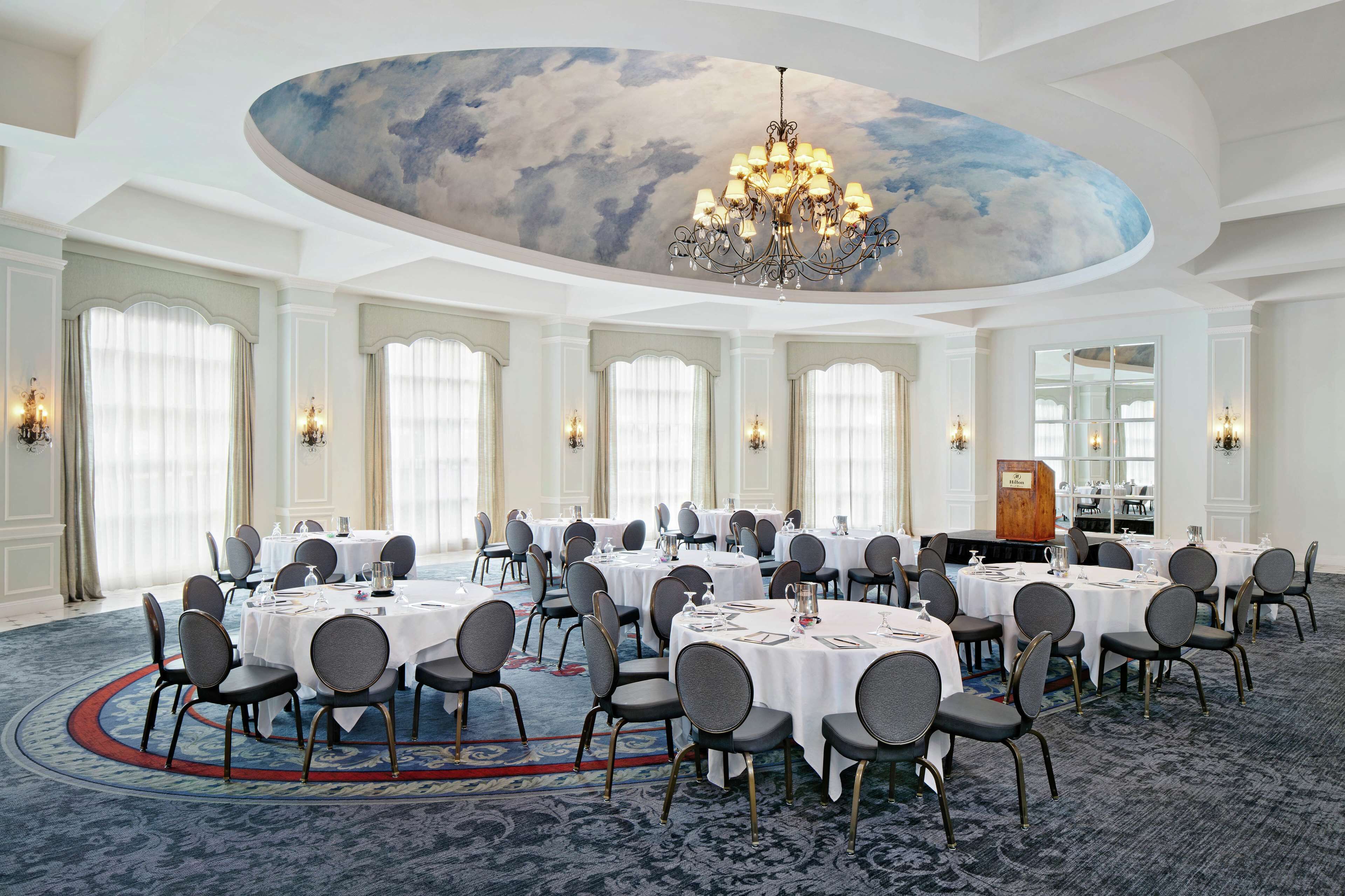 A large conference room with round tables, chairs, and a chandelier.