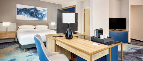 A hotel room with a bed, a desk, a chair, a TV, and a painting on the wall.