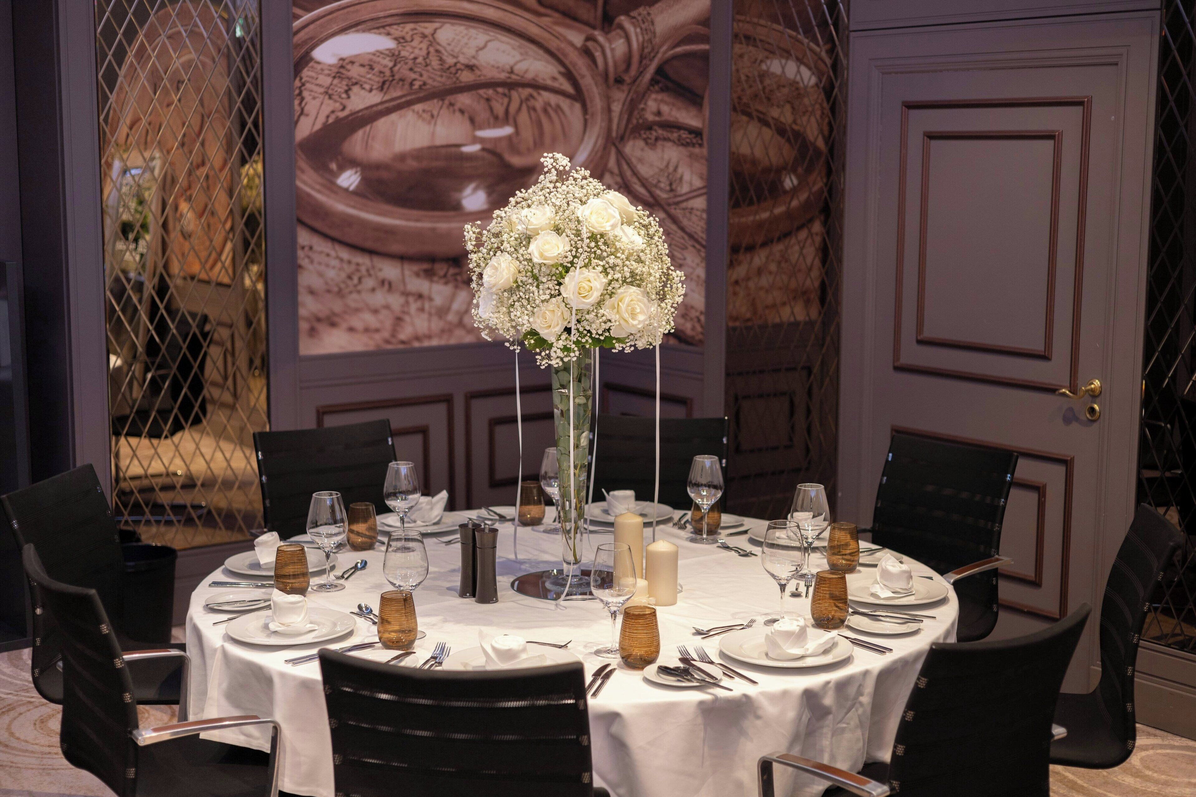 A round dining table with white tablecloth, set with plates, glasses, and a centerpiece of white flowers.