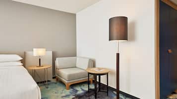 Une chambre d’hôtel avec un lit, une chaise, une petite table, une lampe et une porte.