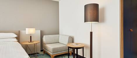 Una habitación de hotel con cama, una silla, una mesita, una lámpara y una puerta.
