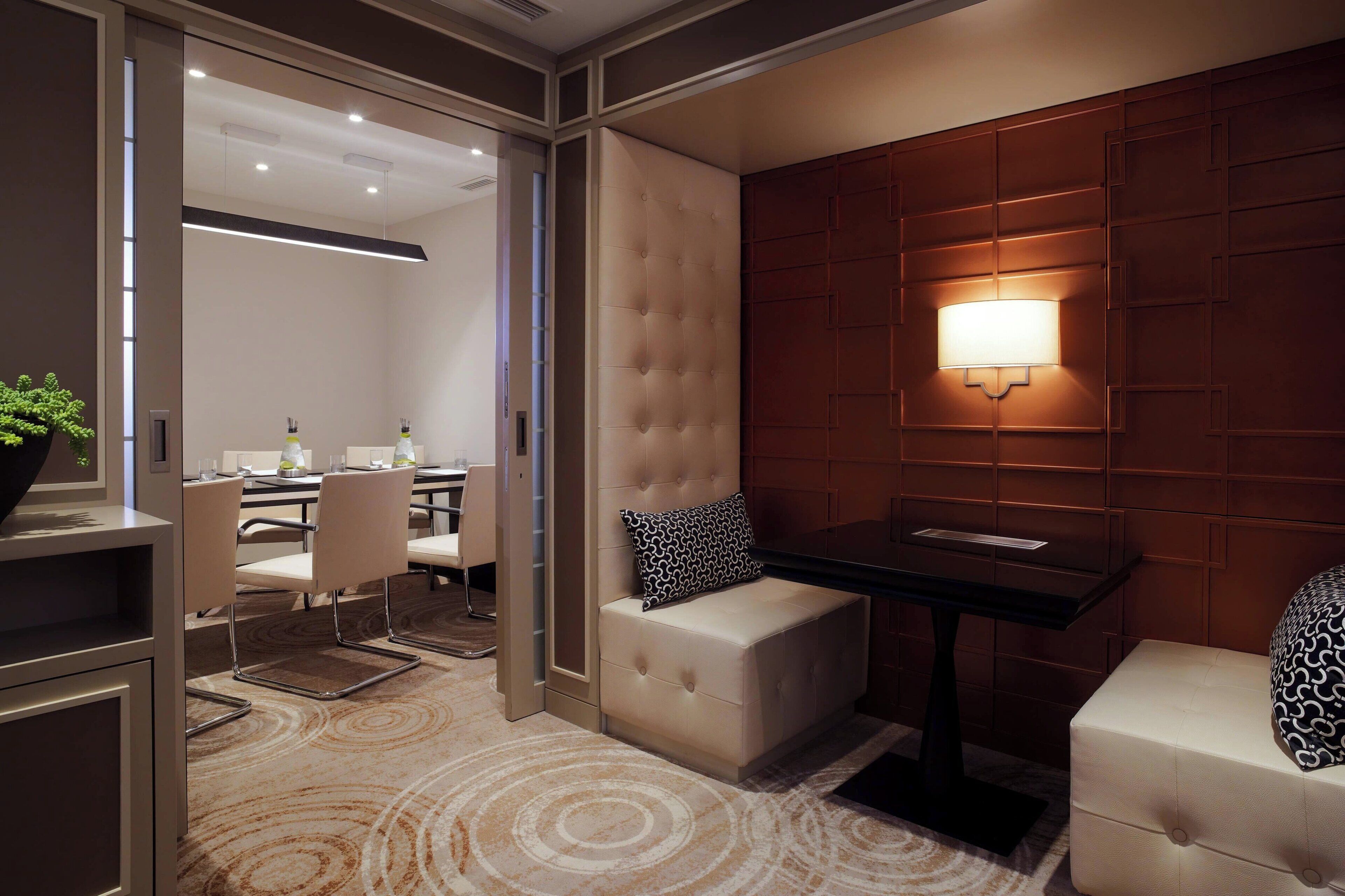 A modern hotel room with a seating area, a table, and a wall-mounted lamp.