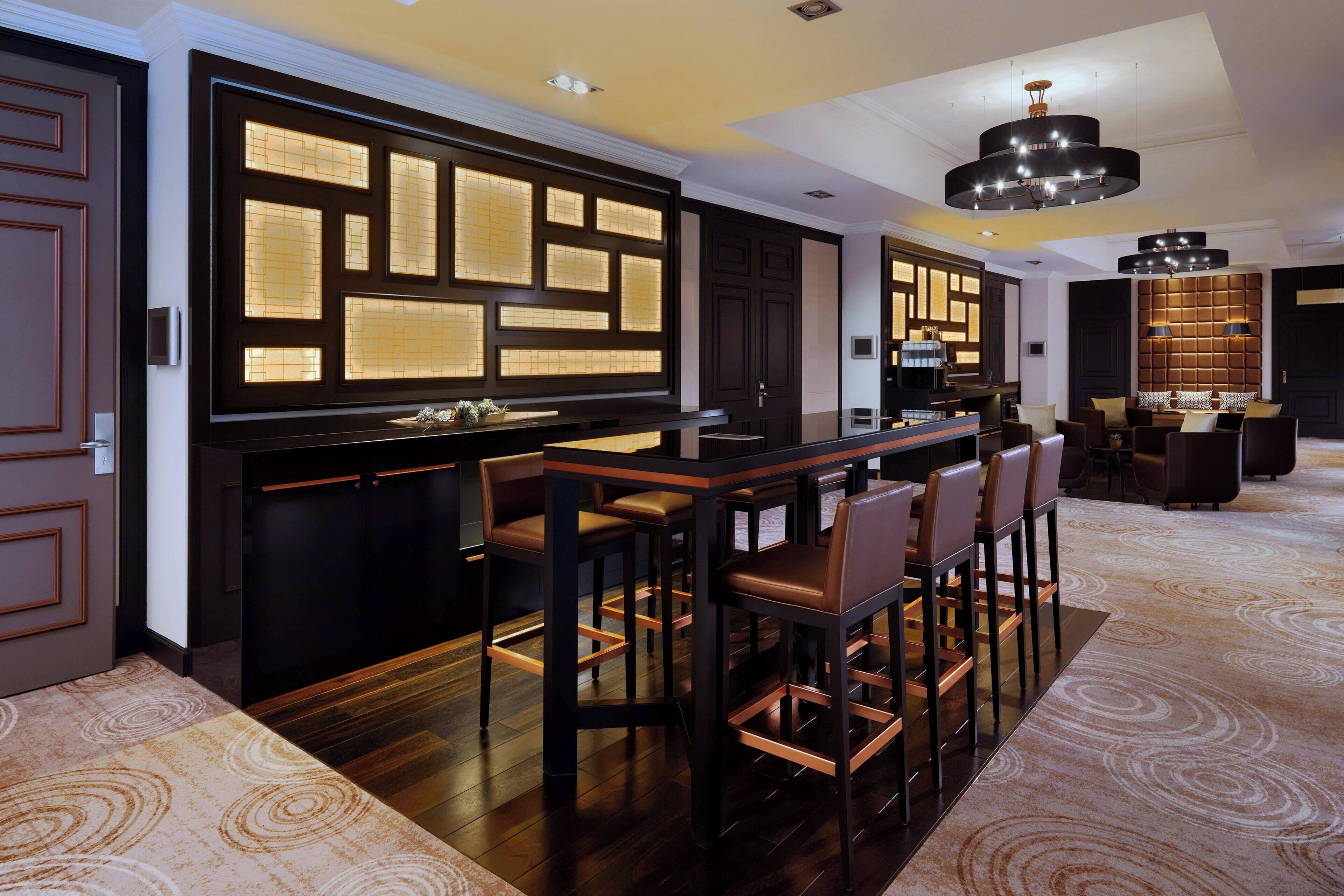 A modern bar area with a dark wood bar, leather bar stools, and a large illuminated screen.