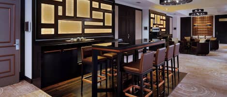 Un área de bar moderna con una barra de madera oscura, taburetes de cuero y una gran pantalla iluminada.