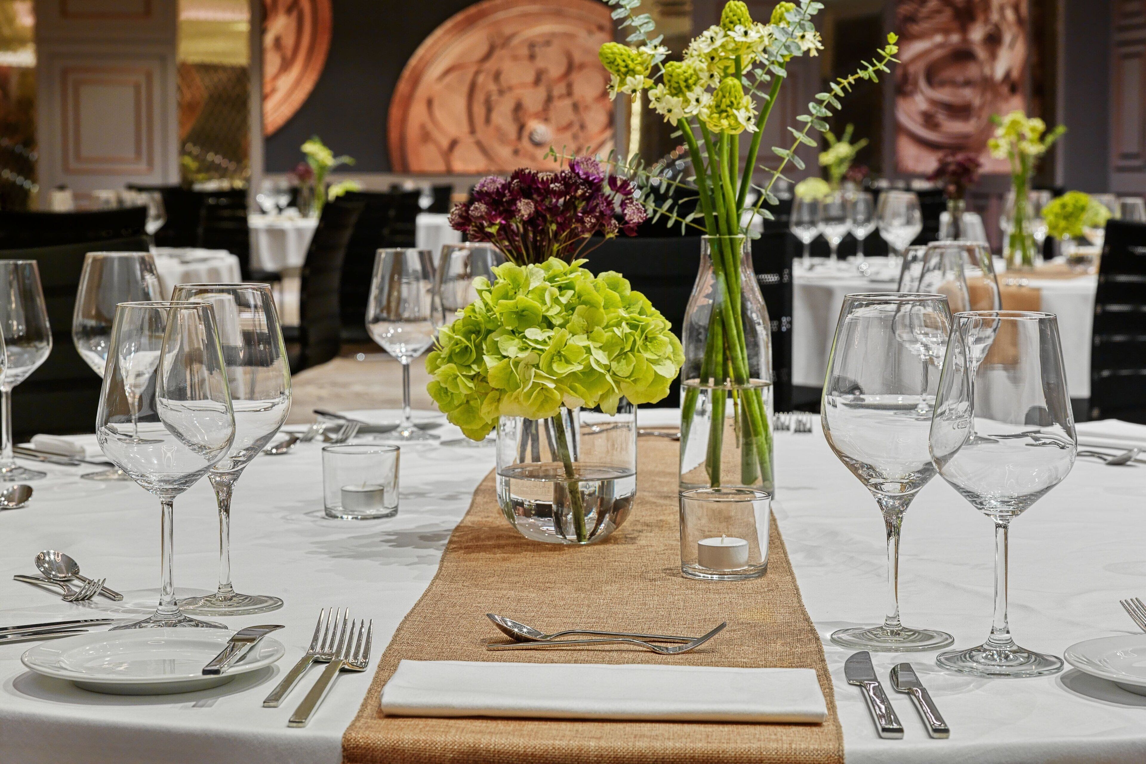 Una mesa preparada para comer, con varias copas de vino, cubiertos y centros de mesa florales.