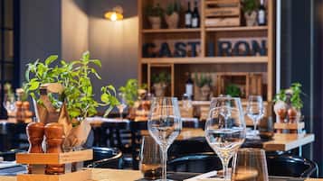 Interior de restaurante con mesas de madera, cristalería transparente y plantas en macetas.