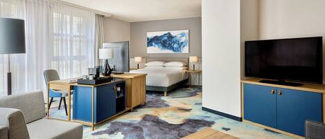A modern hotel room with a bed, a desk, a television, and a sofa.