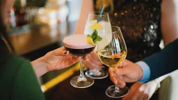 Duas pessoas segurando copos com bebidas, uma com bebida rosa e outra com bebida transparente, em um bar.