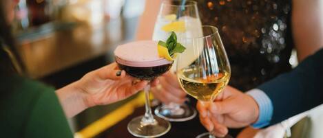 Dos personas sosteniendo vasos con bebidas, uno con un trago rosado y el otro con un trago transparente, en un bar.