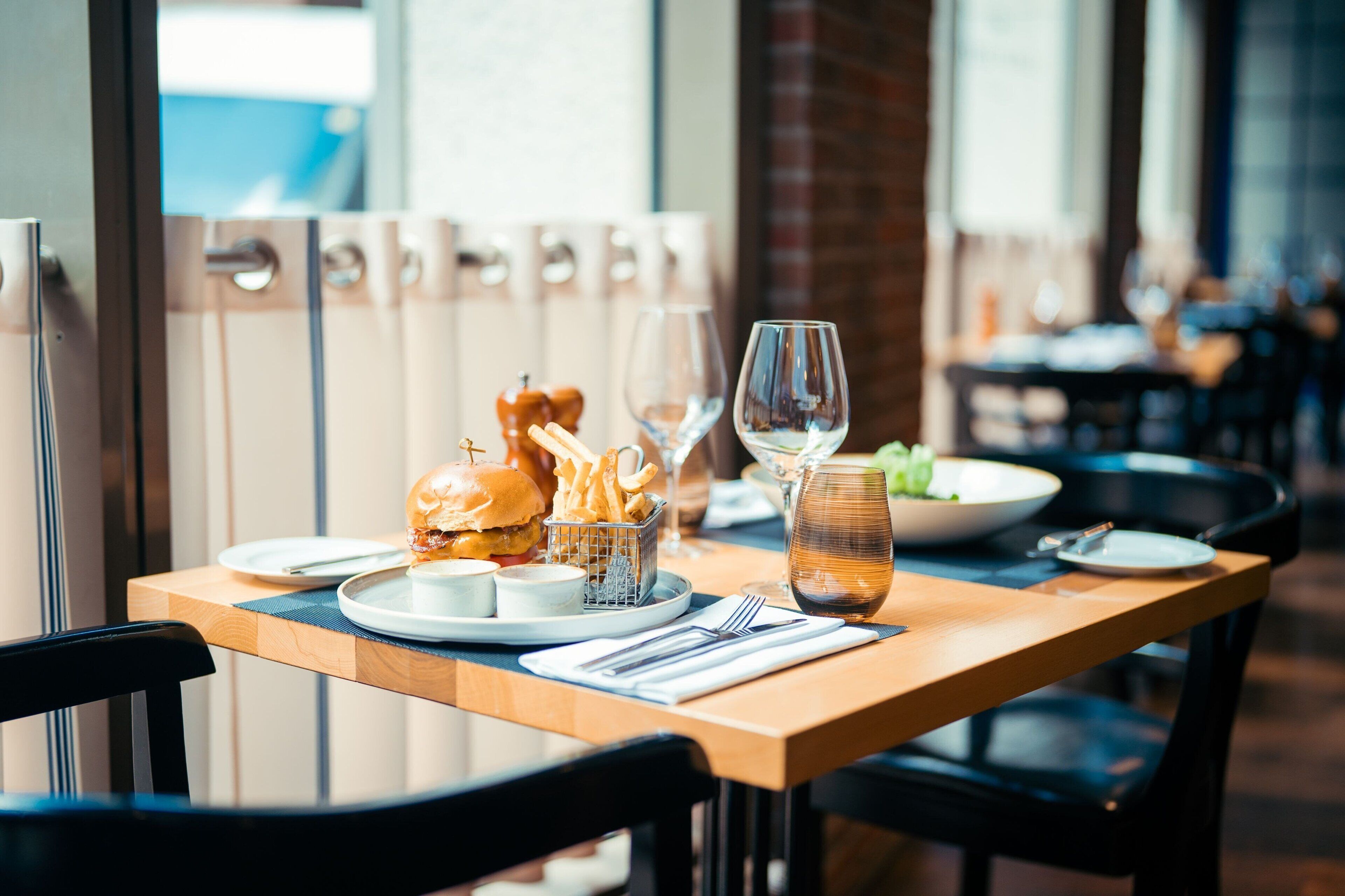 A dining table set with a burger, fries, a glass of wine, and a small bowl of sauce.