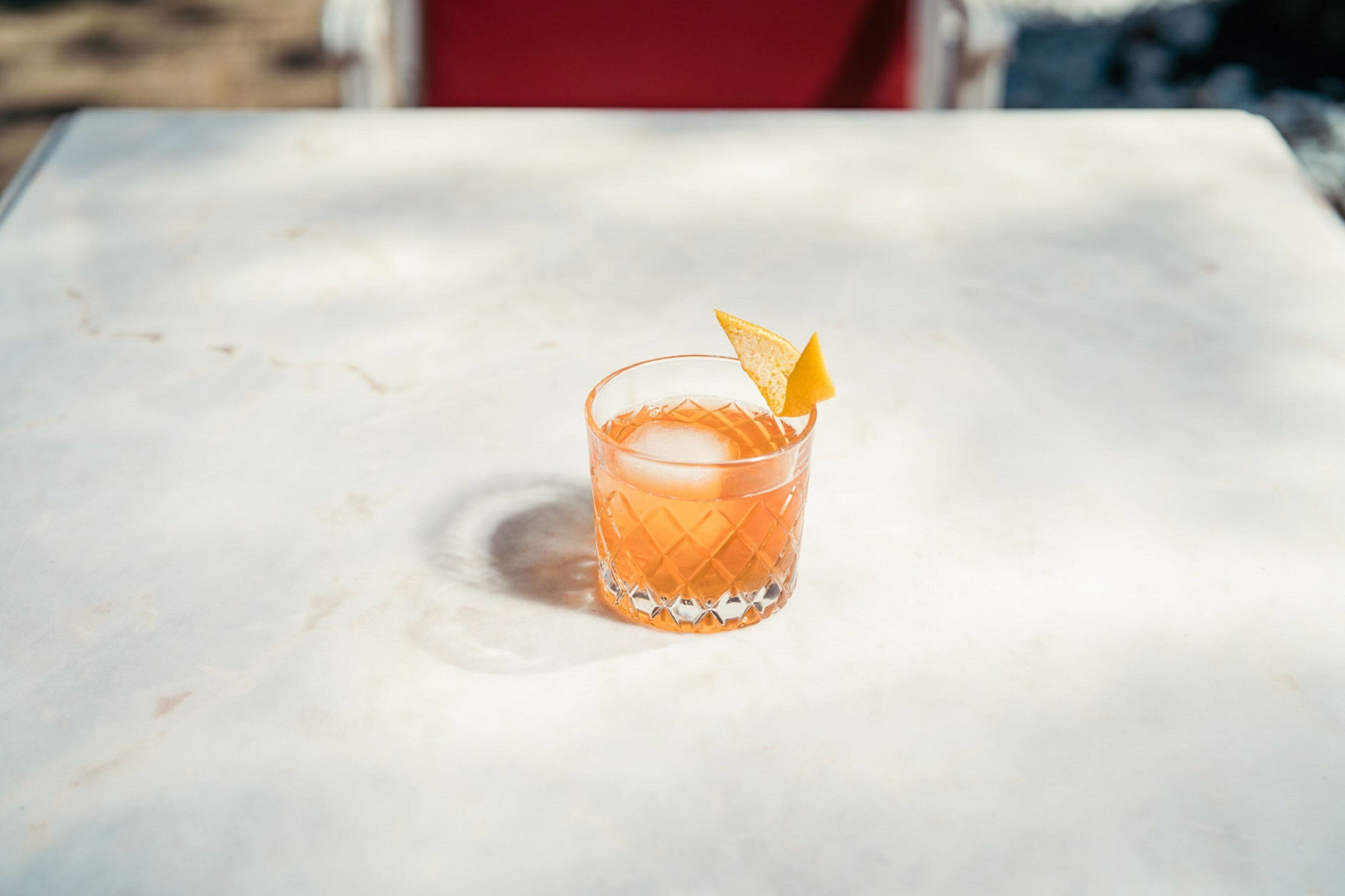 A clear glass with a textured pattern, containing a beverage and a garnish, on a white surface.