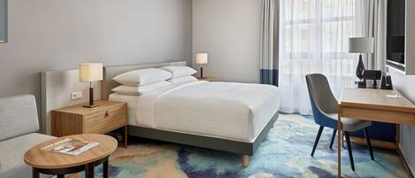 A hotel room with a bed, a desk, a chair, a small table, and a sofa.