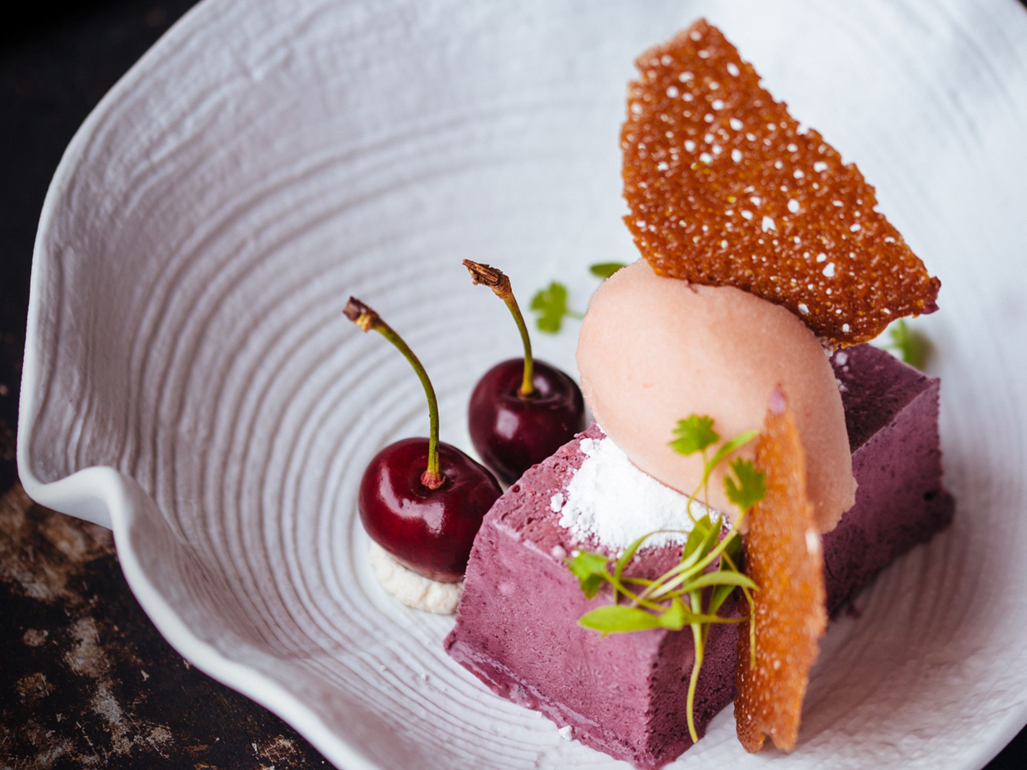 A dessert plate with a scoop of ice cream, two cherries, and a piece of cake.