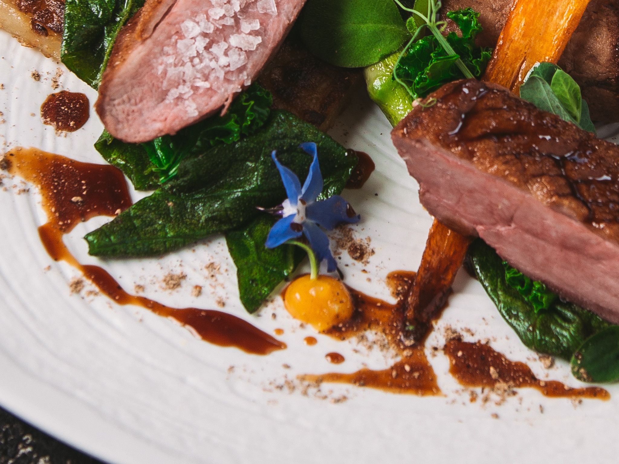 A plate of food with various ingredients including greens, a slice of meat, and a small flower.