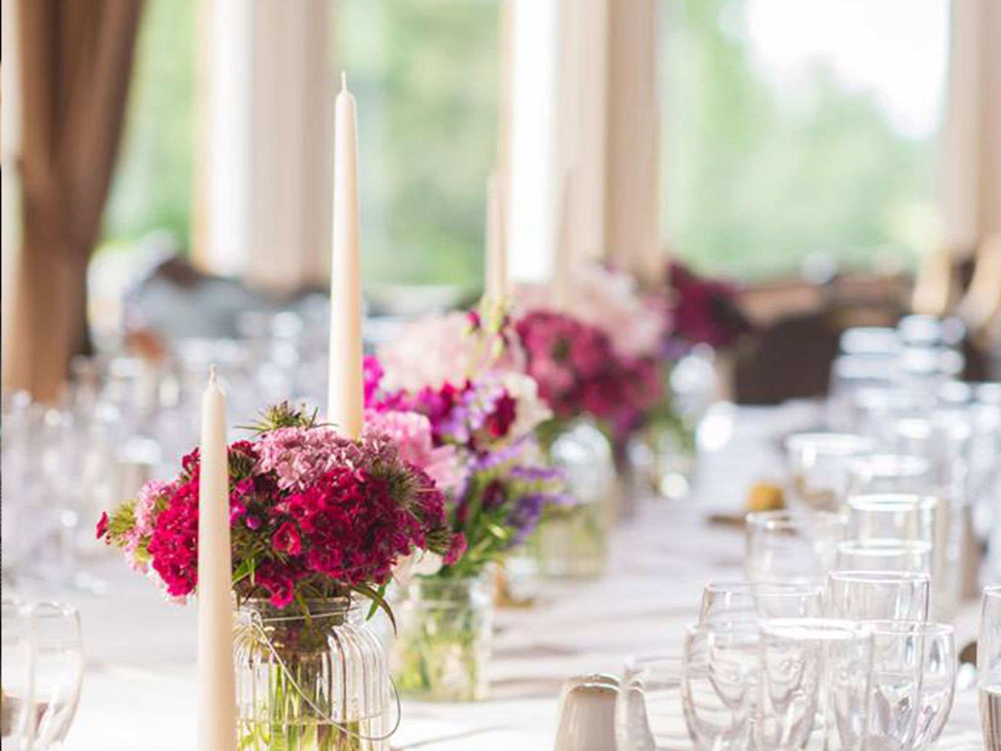 A table set with clear glassware and vases containing pink flowers.