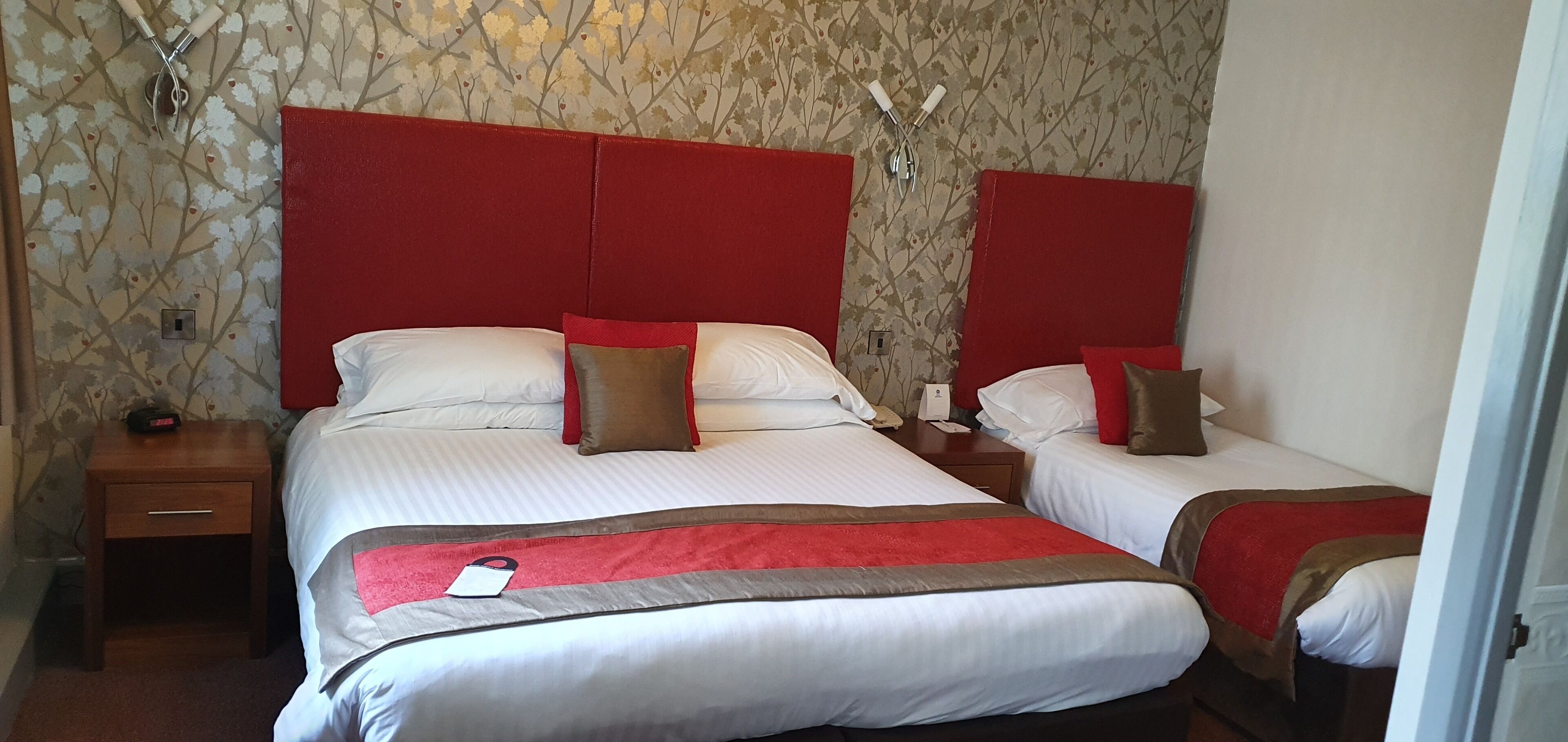 Ett hotellrum med två sängar, var och en med röda sänggavlar, vita sängkläder och bruna kuddar. Det finns ett nattduksbord med en telefon och ett litet bord mellan sängarna.