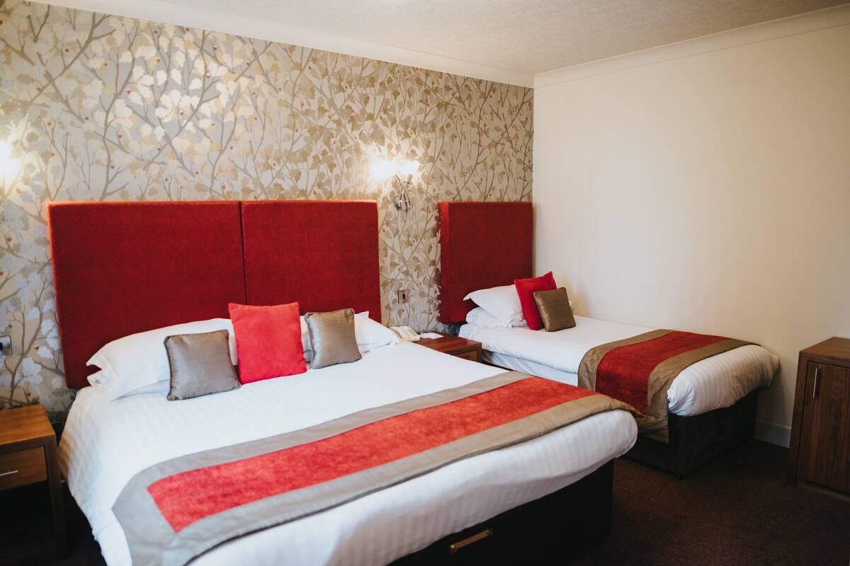 A hotel room with two beds, red headboards, and a floral wallpaper pattern.