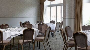 A dining area with tables set for a meal, chairs, and a view through large windows.
