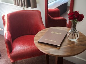 A red leather armchair, a wooden table with a guest information booklet, and a vase with red roses. - Oaklands Hall Hotel Grimsby (Grimsby)