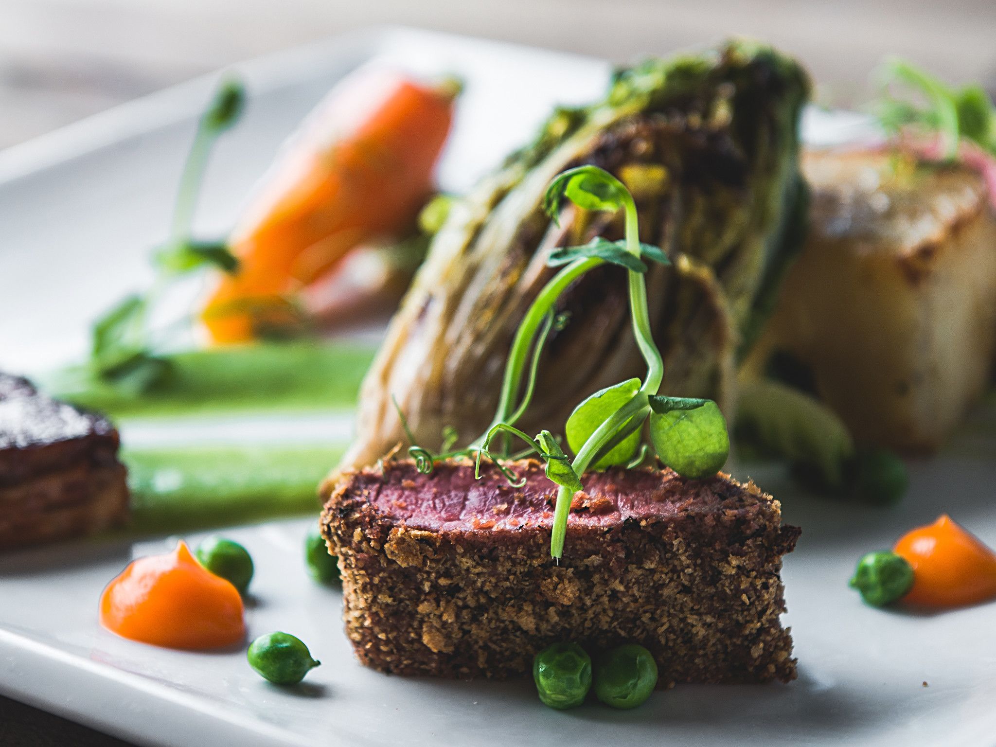 A plate with a slice of meat, asparagus, and peas.