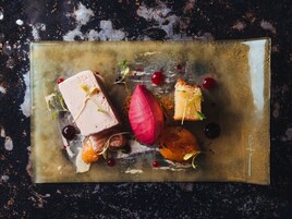 A rectangular plate with various food items including a piece of cake, a red fruit, and some berries, arranged on a textured surface.
