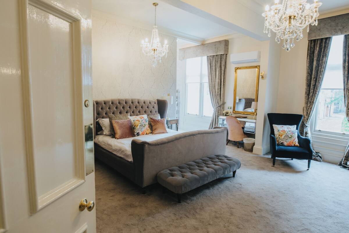 A bedroom with a large bed, a bench, a chair, a desk, and a chandelier.