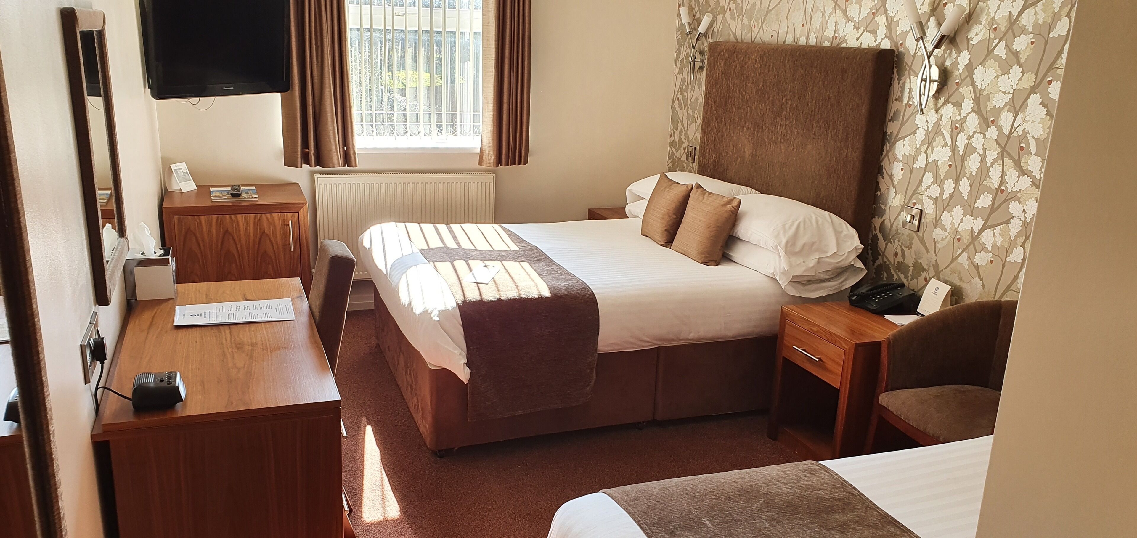 A hotel room with a bed, a desk, a chair, a TV, and a window with curtains.