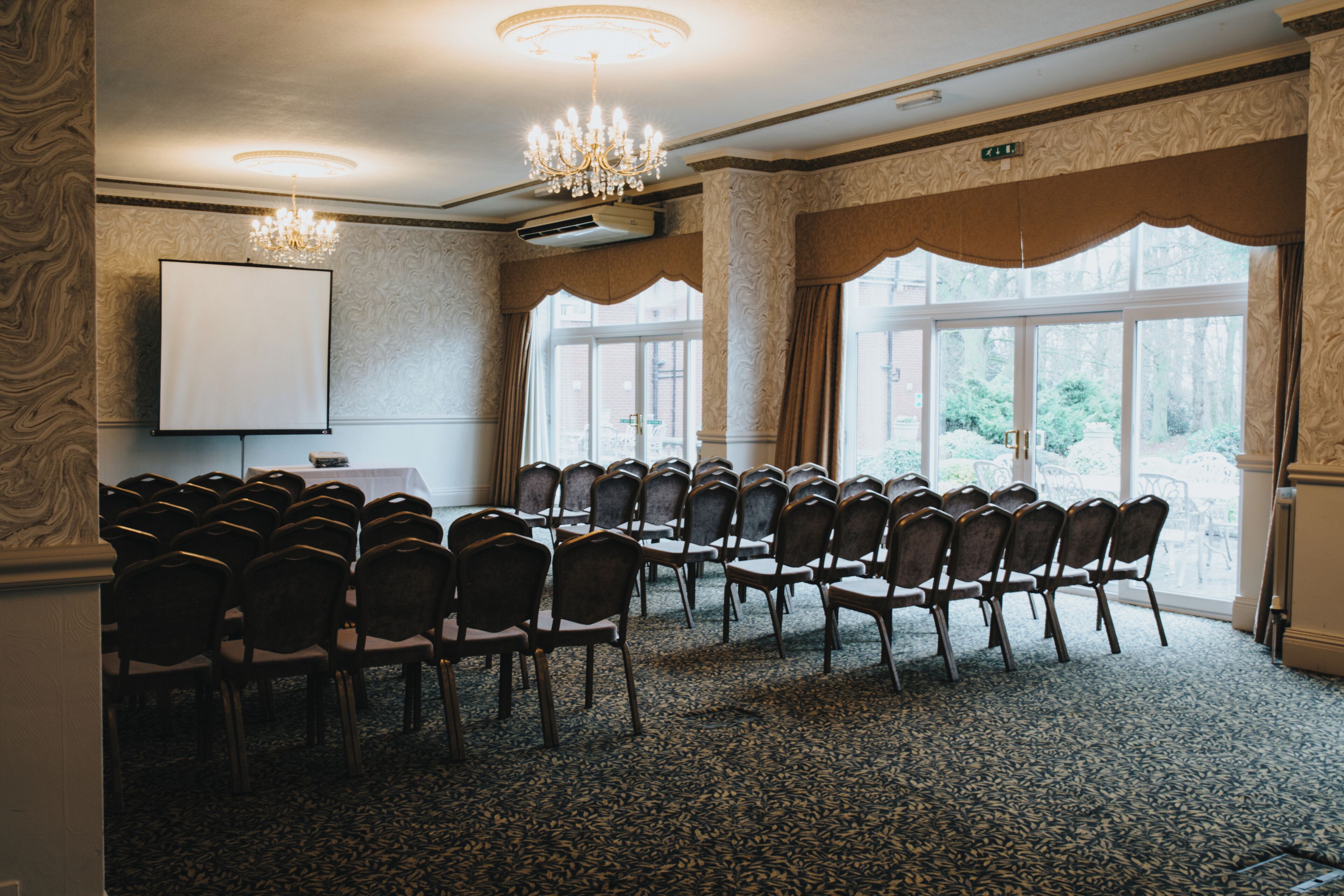 A conference room with rows of chairs, a projector screen, and large windows with curtains.