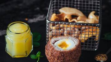A scotch egg, a jar of sauce, and a basket of fried items on a dark surface.