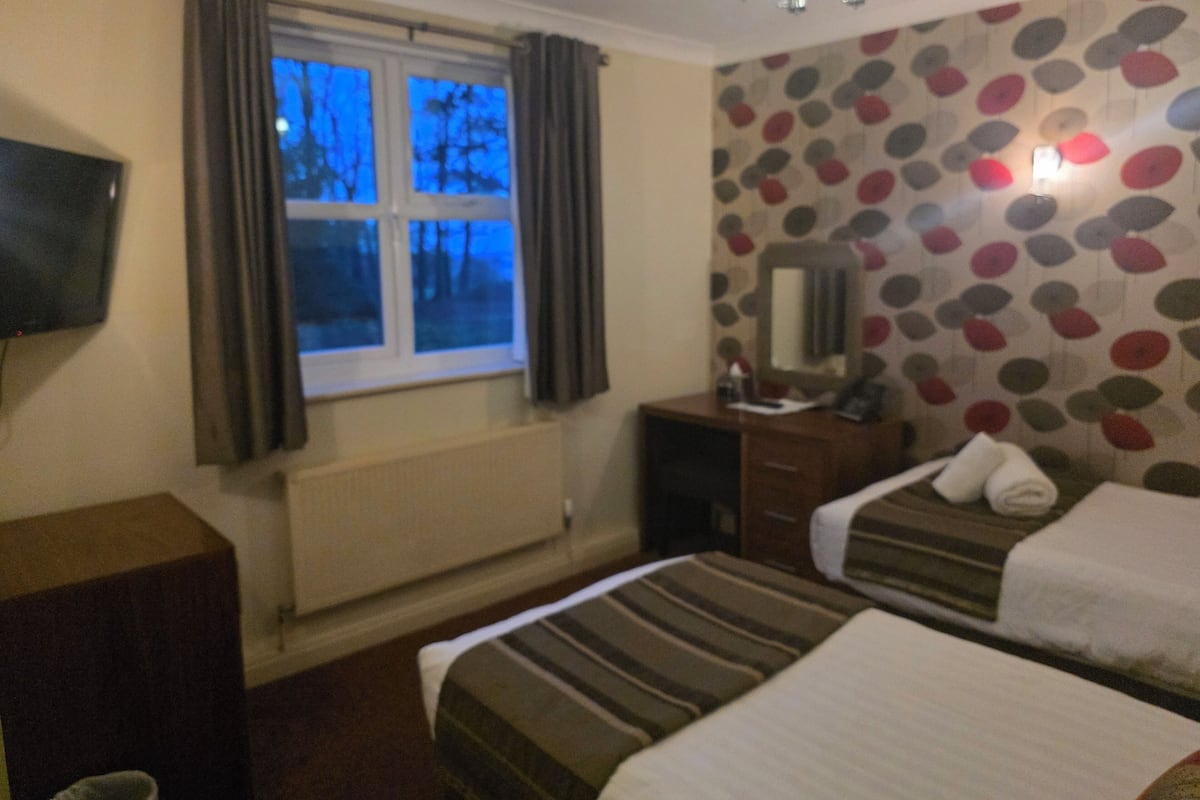 A hotel room with two beds, a TV, a dresser, and a window with curtains.