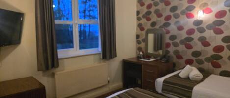 Een hotelkamer met twee bedden, een televisie, een kaptafel en een raam met gordijnen.