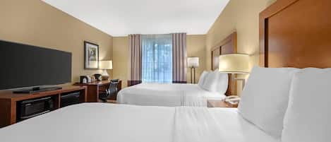 Habitación de hotel con dos camas, televisión, escritorio con lámpara y ventana con cortinas.