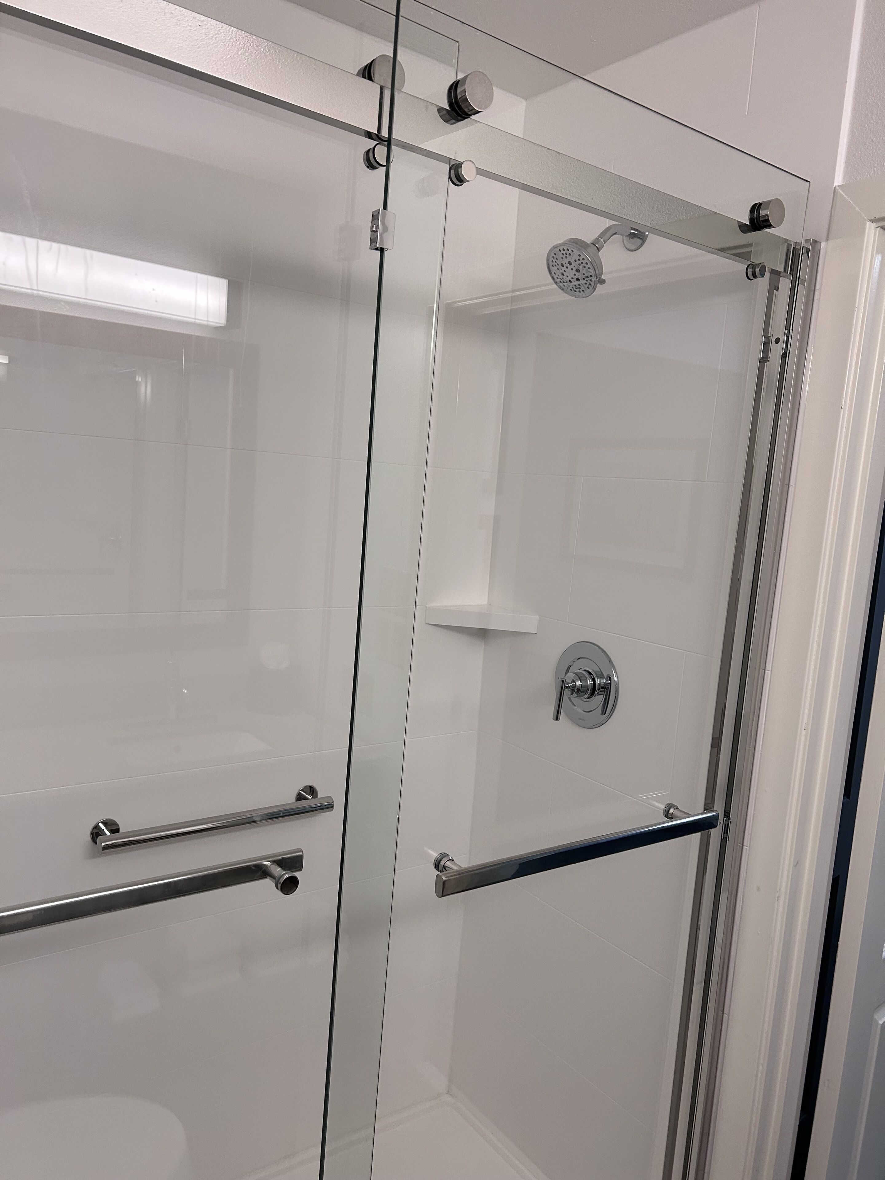 A glass-enclosed shower with a handheld showerhead, a wall-mounted faucet, and a glass door with a handle.