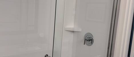 A glass-enclosed shower with a handheld showerhead, a wall-mounted faucet, and a glass door with a handle.