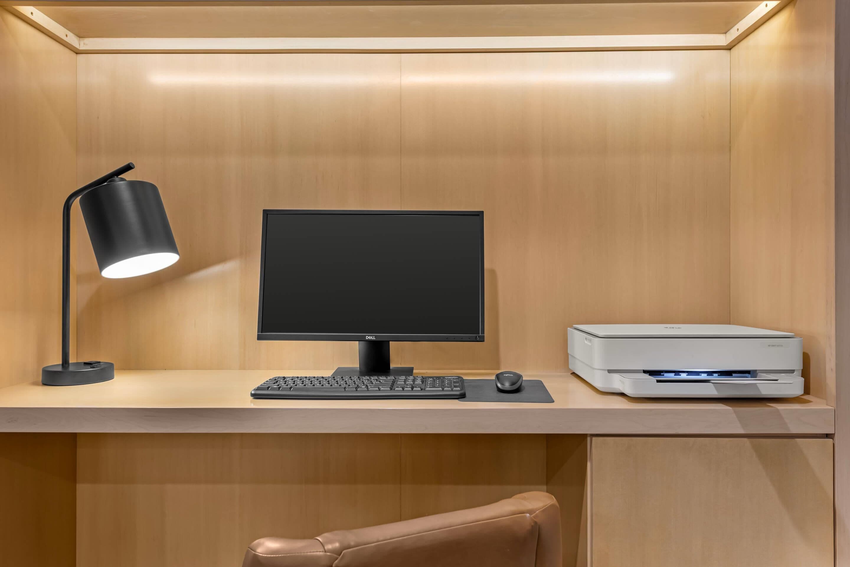 A modern office desk with a Dell monitor, a keyboard, a mouse, a black desk lamp, and a white printer.