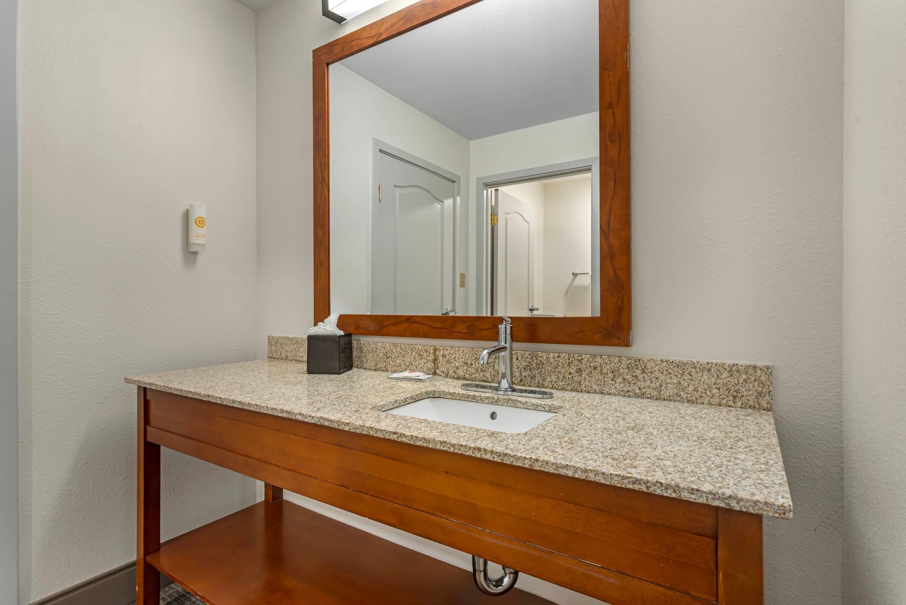 A bathroom with a granite countertop sink, wooden vanity, and a large mirror.
