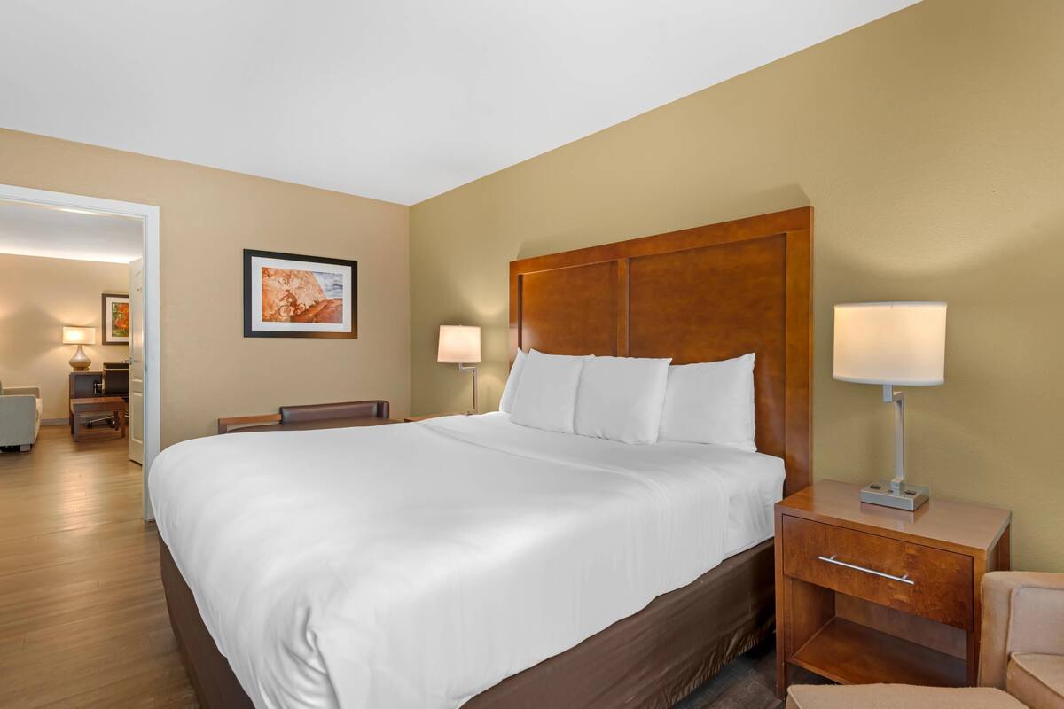 A hotel room with a large bed, two bedside tables with lamps, a wooden headboard, and a framed picture on the wall.