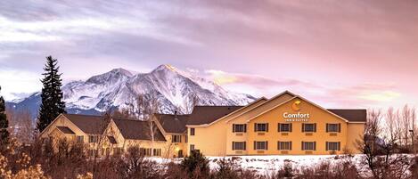 A hotel with a mountain backdrop, featuring a large building with multiple windows and a sign reading "Comfort Inn & Suites".