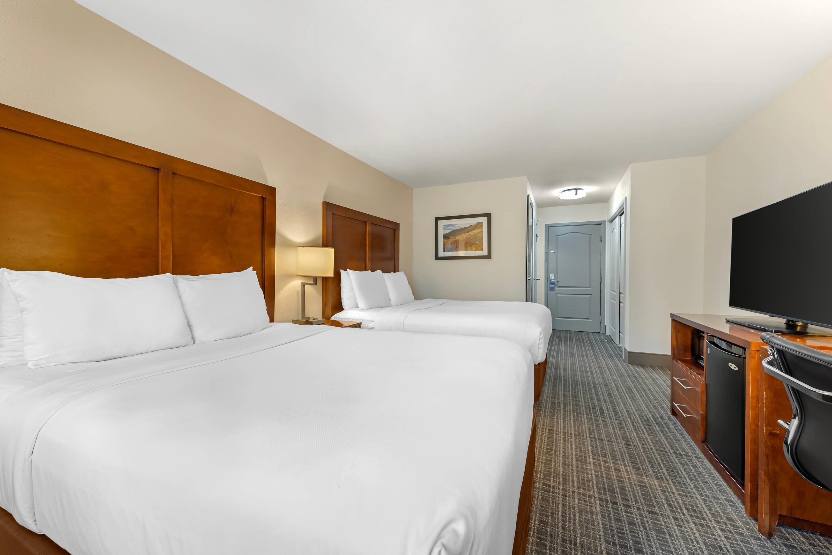 A hotel room with two beds, a desk, a television, and a door leading to the bathroom.