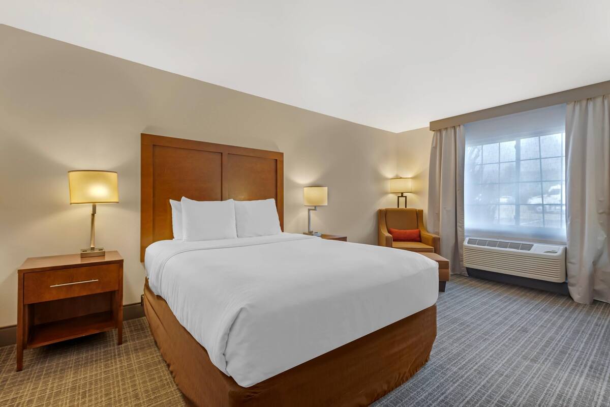 A hotel room with a large bed, two bedside tables with lamps, a chair, and a window with curtains.