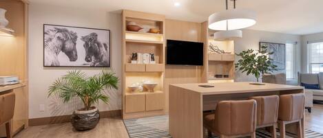 Una cocina moderna con una isla central, armarios de madera, un televisor de pantalla plana y una planta grande en maceta.