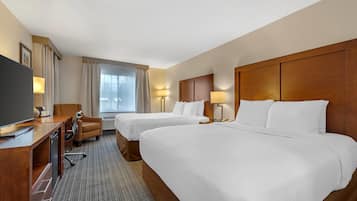 Habitación de hotel con dos camas, un escritorio, un televisor, una silla y una ventana con cortinas.