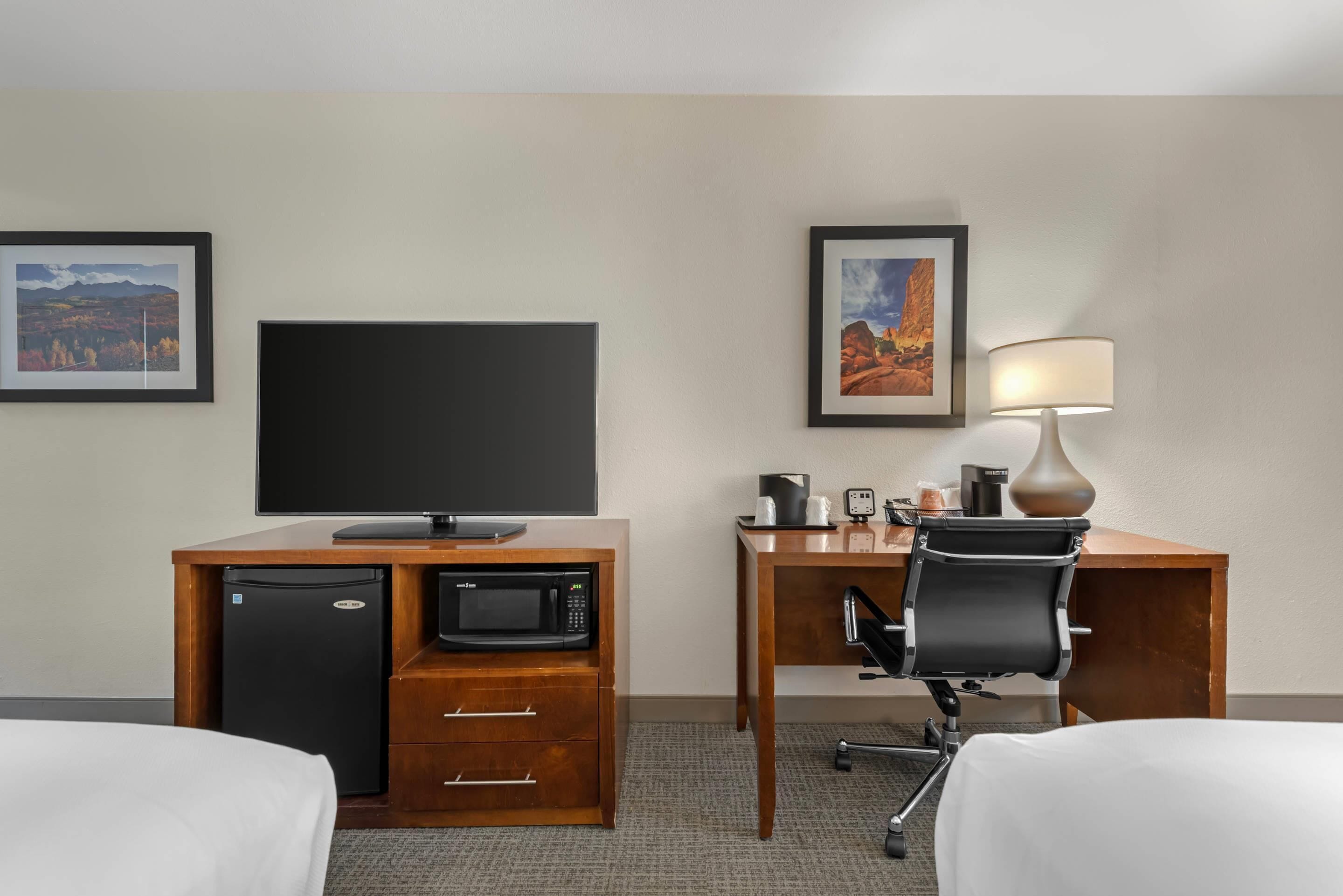 Una habitación de hotel con cama, escritorio, computadora, microondas y televisor.