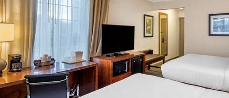 Une chambre d’hôtel comprenant un lit, un bureau avec une chaise, une télévision et un minibar.