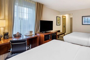 A hotel room with a bed, a desk with a chair, a television, and a minibar.