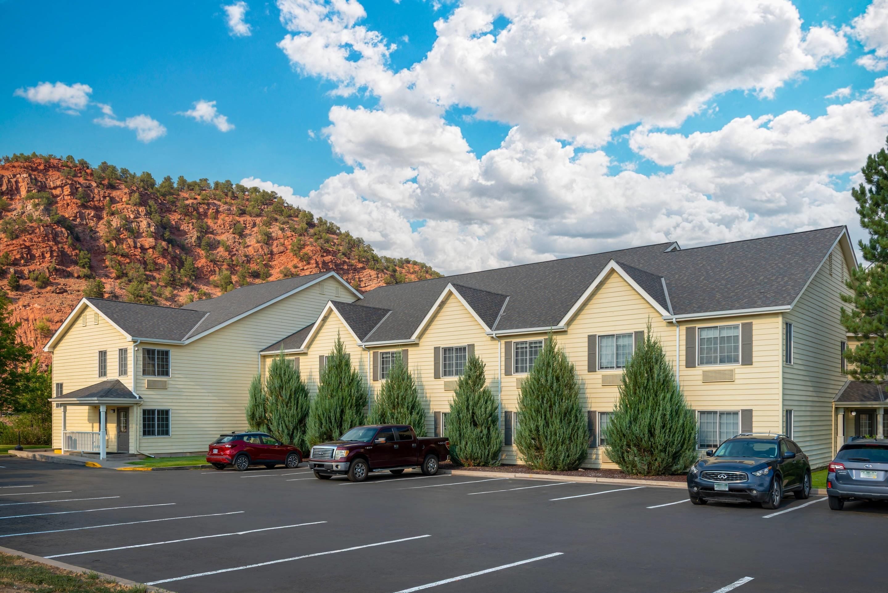 A hotel with multiple units, a parking lot, and a mountainous backdrop.