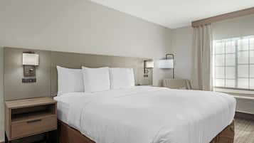 Habitación de hotel con una cama grande, una mesita de noche, una lámpara y una ventana con cortinas.