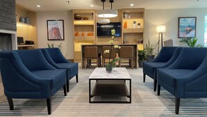 A modern living room with two blue armchairs, a coffee table, and a dining area with a TV.